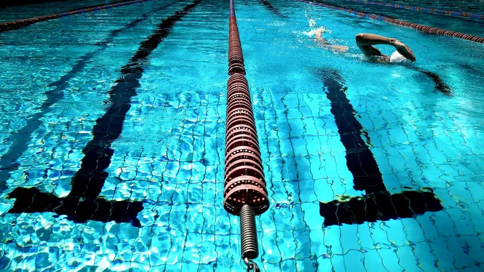 Clear turquoise swimming pool water with a lane rope and a swimmer in the distance