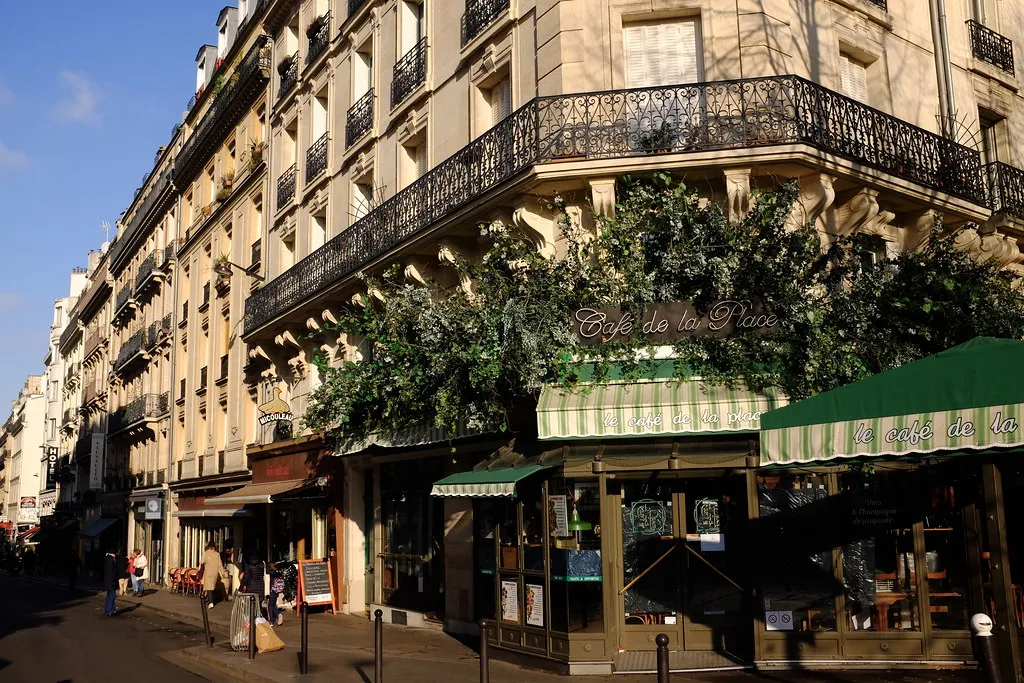 A Paris corner cafe with green awnings beneath a cream stone building with wrought-iron balconies