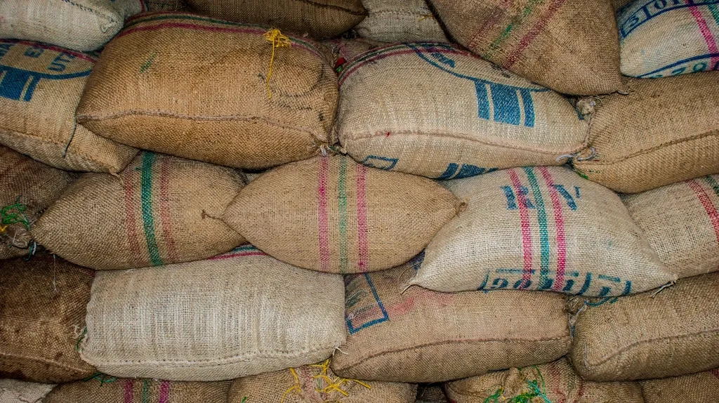 Burlap sacks of coffee with faded stencilled stripes stacked tightly in a warehouse