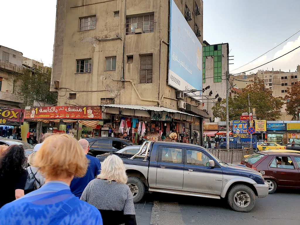 A busy downtown street in Amman lined with shops, with a pickup truck in traffic