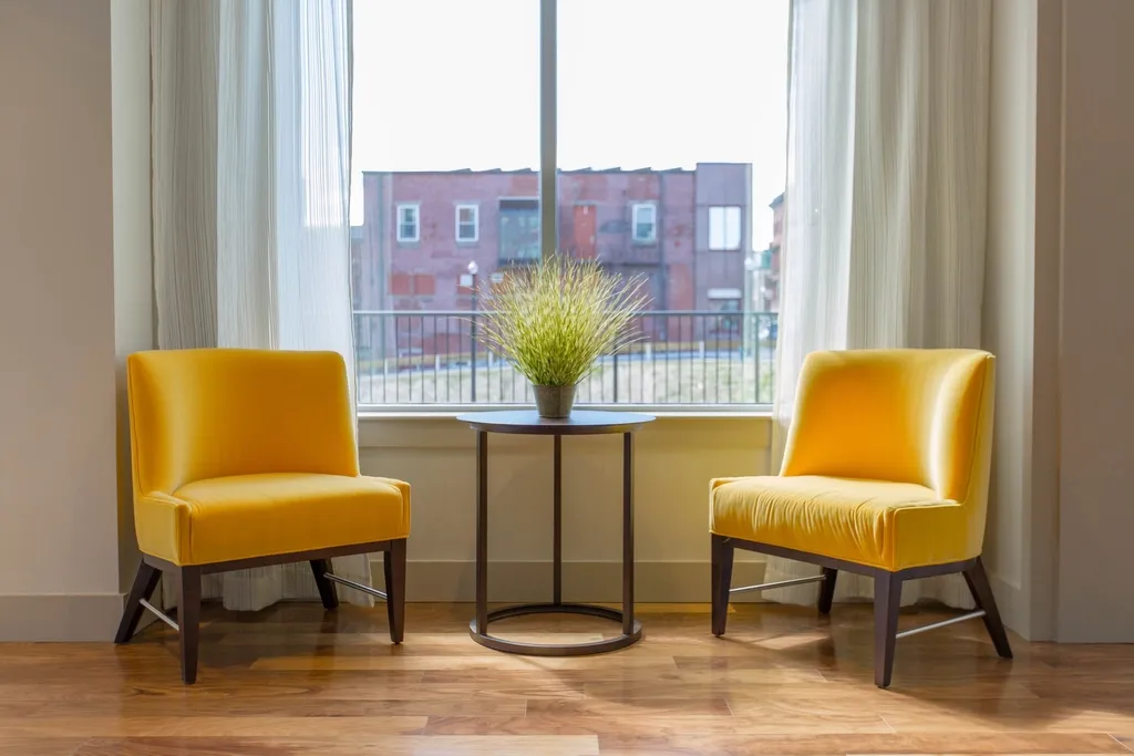 Two yellow padded armchairs facing a window with a small round table between them