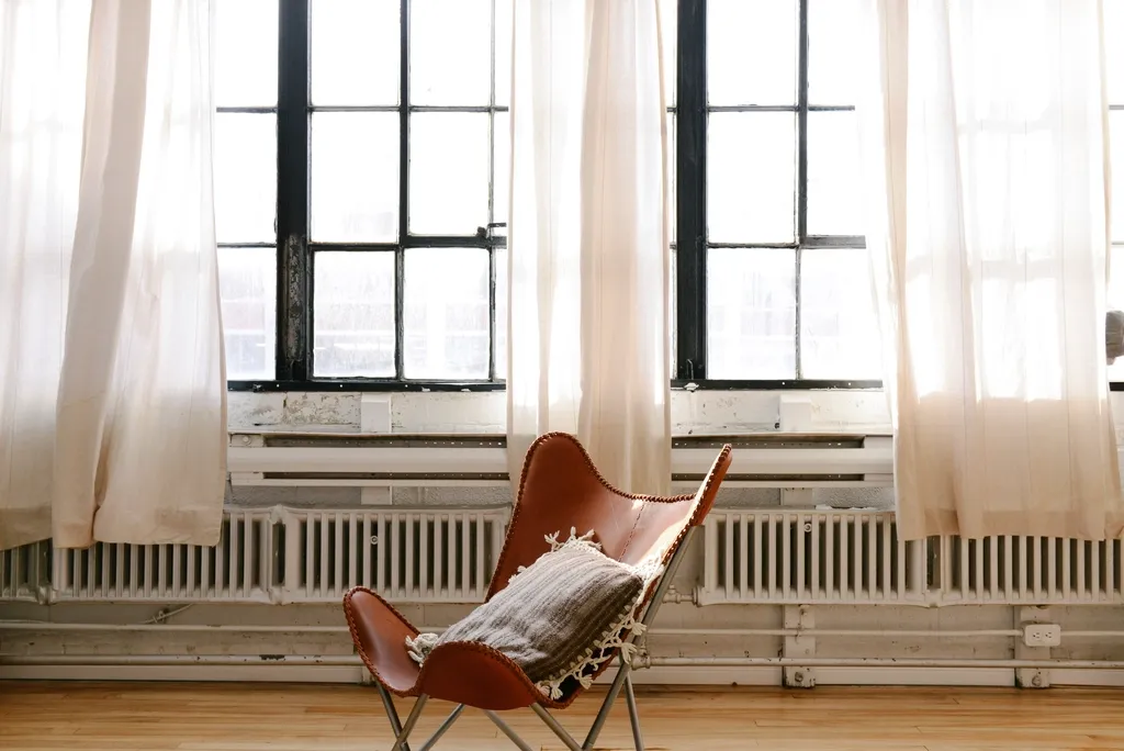 A brown leather sling chair in front of tall windows with sheer white curtains