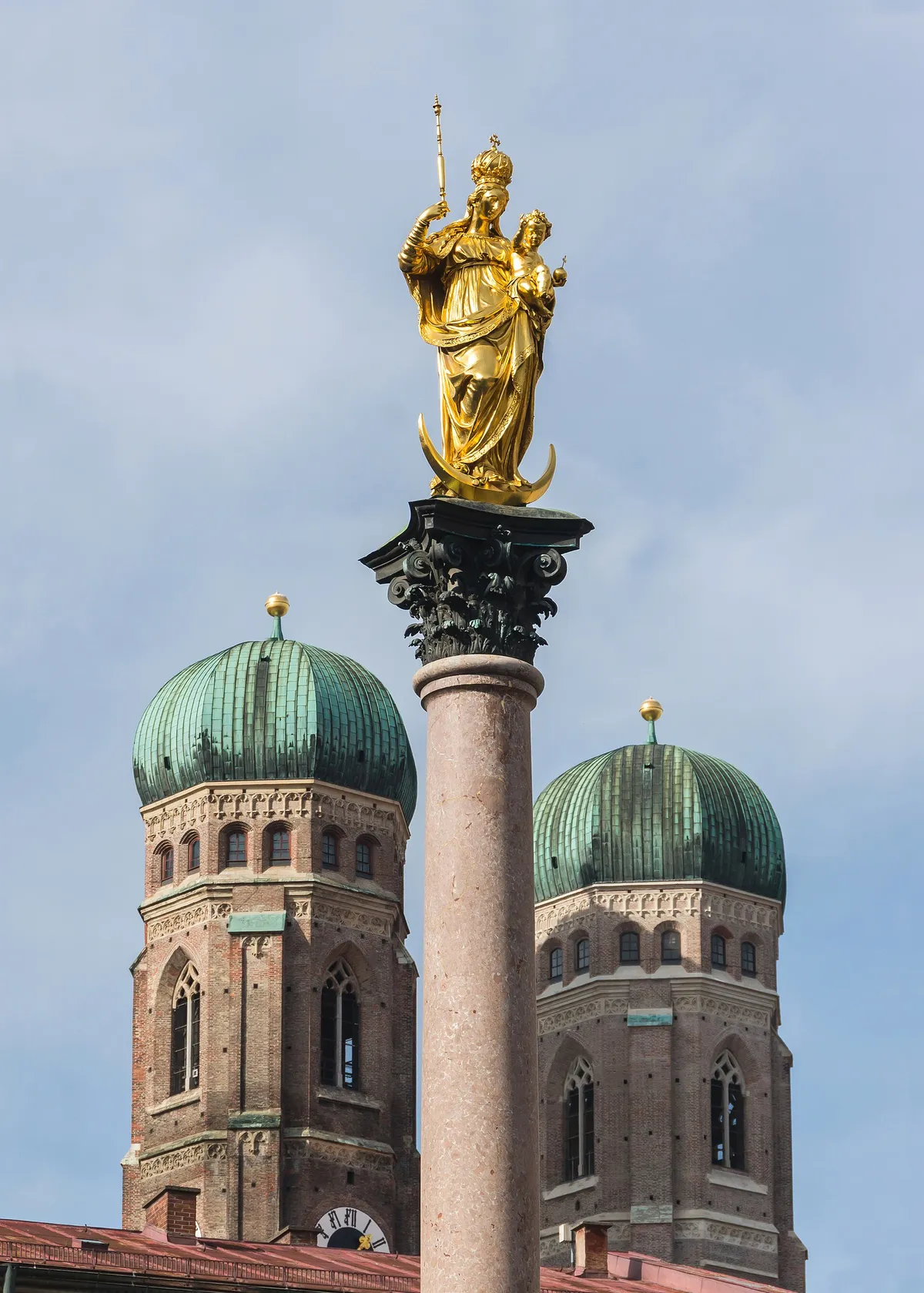 A golden statue on a column in front of the twin domed towers of the Frauenkirche in Munich
