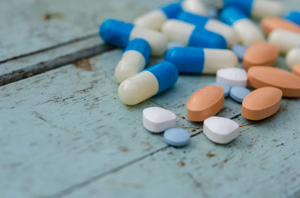 Blue-and-white capsules and orange tablets scattered on a wooden table