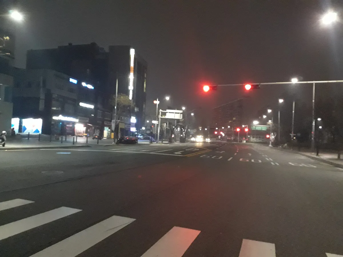 An empty city street with crosswalk stripes and a red traffic light before dawn in Seoul