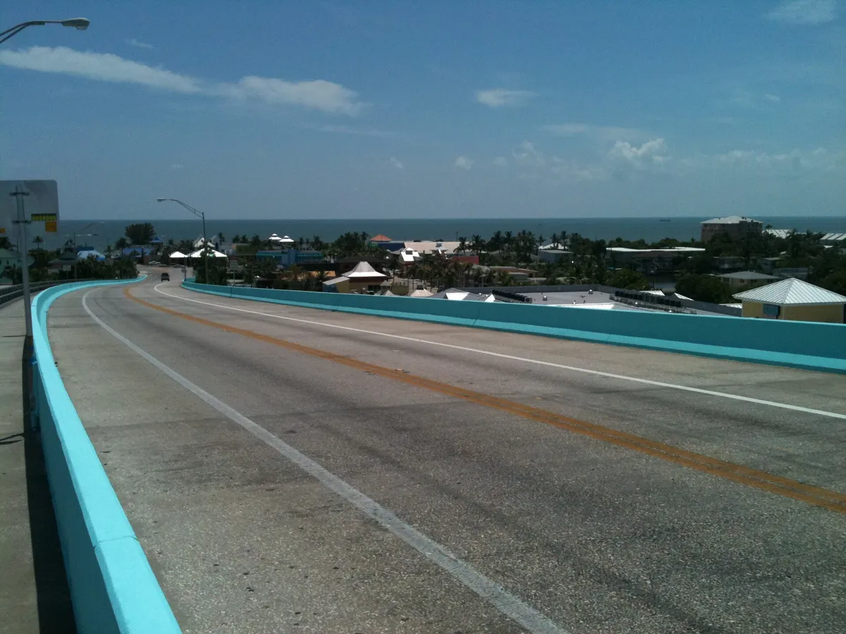 A two-lane bridge road with turquoise railings leading toward Fort Myers Beach and the Gulf of Mexico