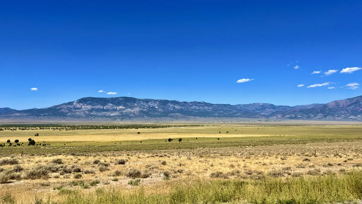 A wide Nevada valley of dry grass and sagebrush under a deep blue sky with mountains on the horizon