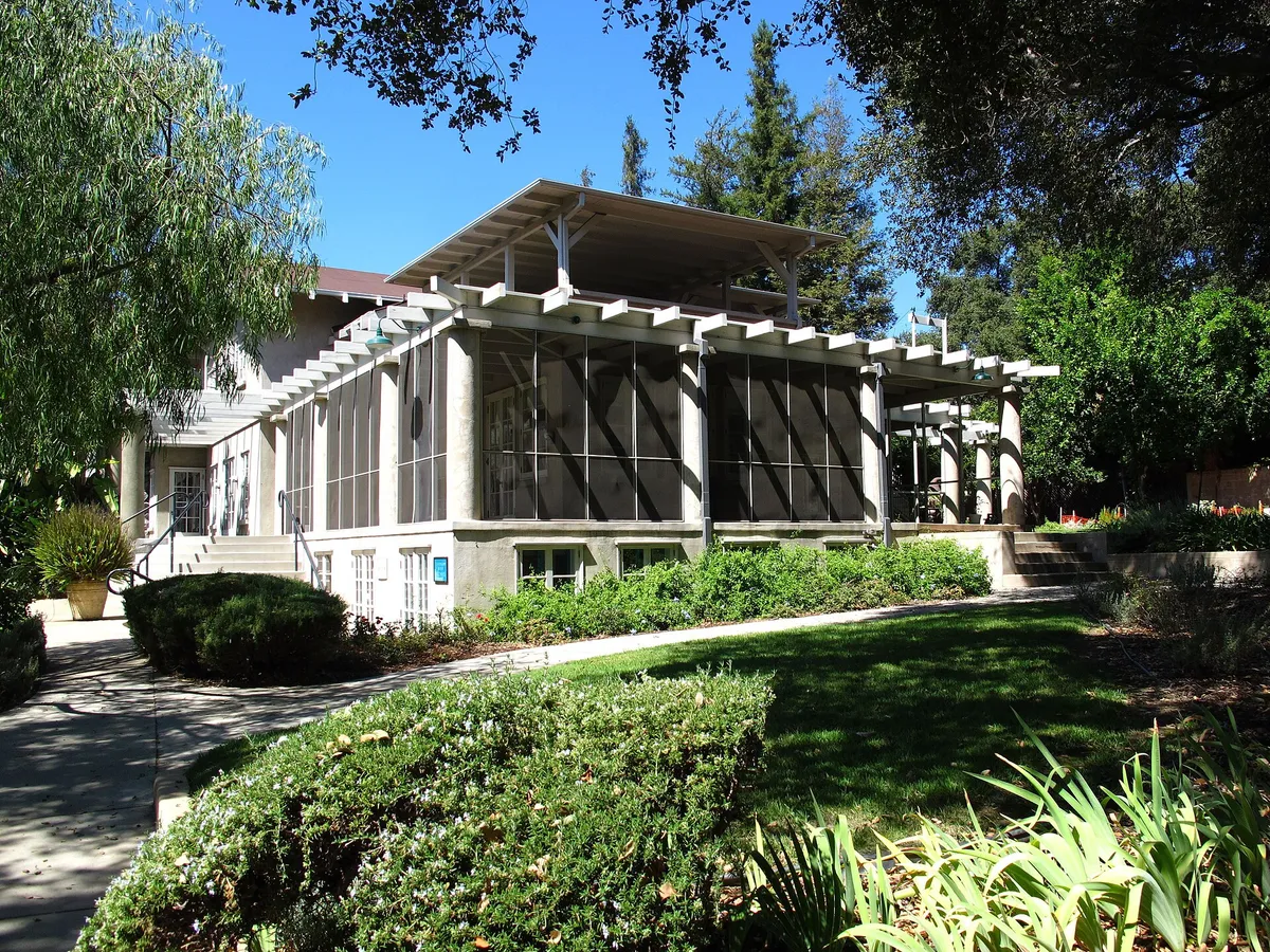 A screened porch with white framing on a house surrounded by green shrubs and trees
