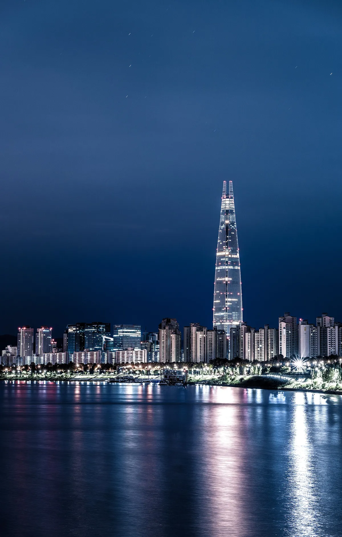 A tall illuminated tower rising above apartment blocks in Seoul at night