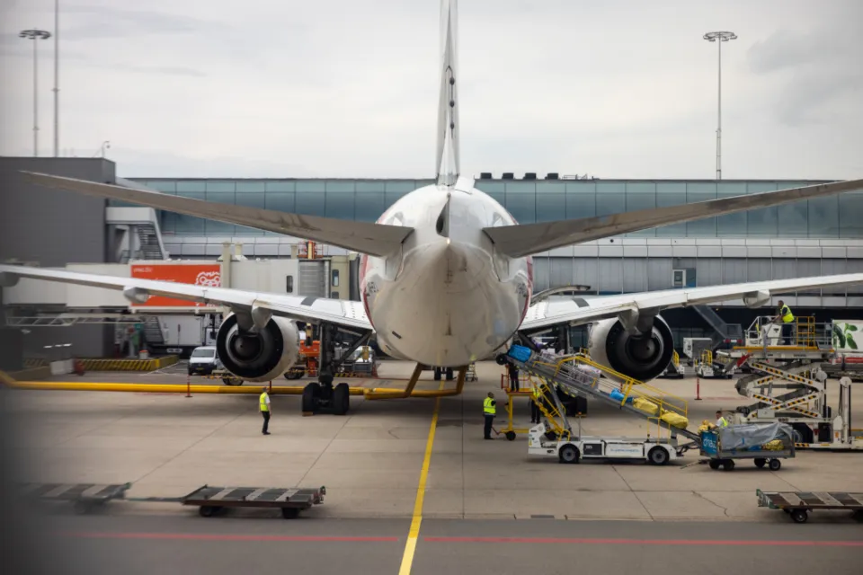 A wide-body airliner parked at an airport gate with baggage loaders and ground crew around it