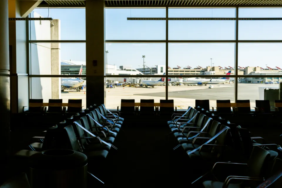 Rows of empty seats in an airport terminal facing tall windows