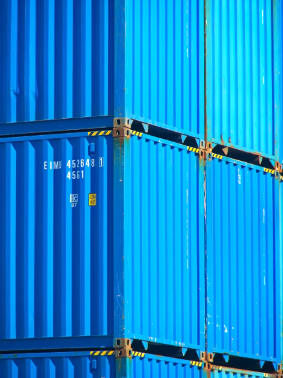 Close-up of stacked blue shipping containers with an identification number painted on the side