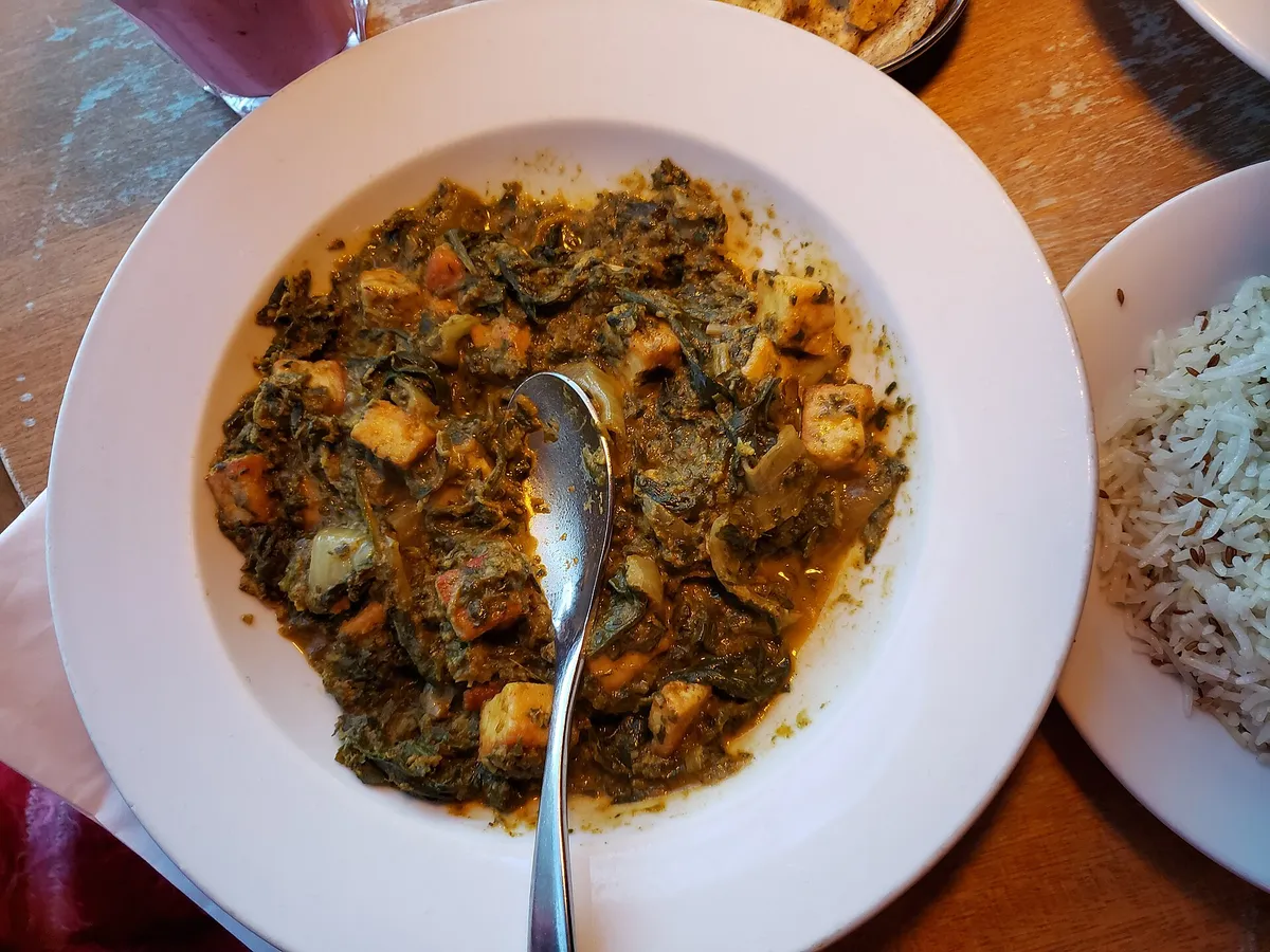A bowl of spinach and paneer curry beside a plate of white rice