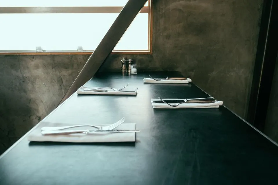 A long, empty dining table set with folded napkins in a softly lit room