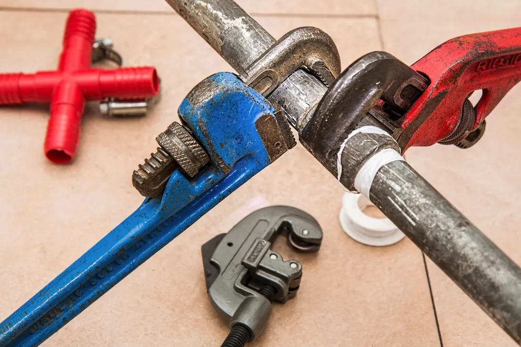 Red and blue pipe wrenches gripping metal plumbing pipes on a tiled floor