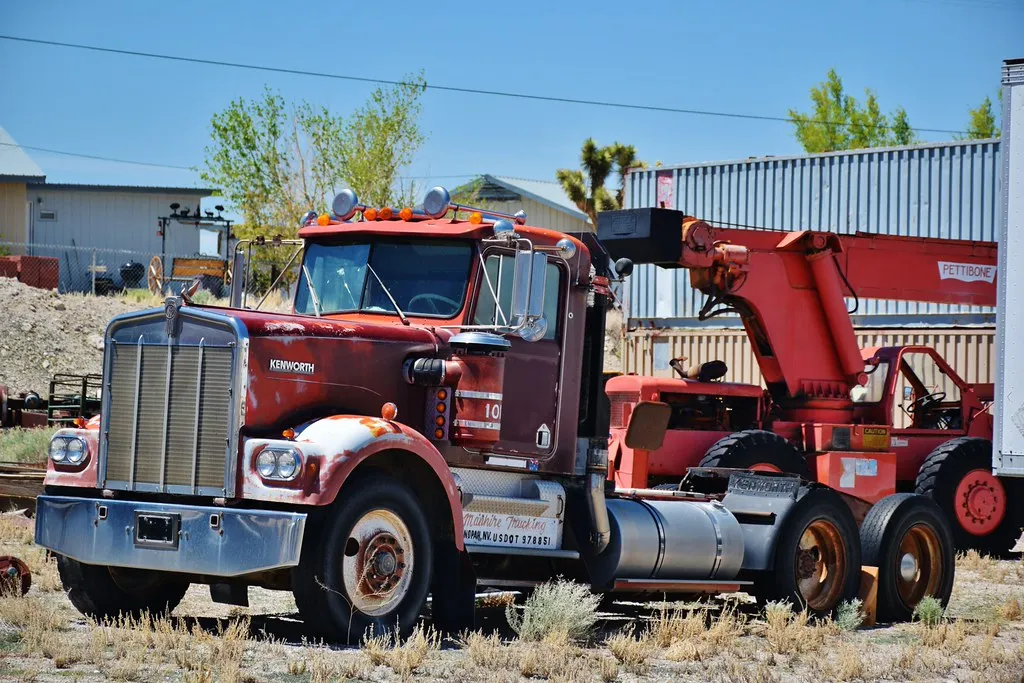 An old red heavy tow truck parked in a gravel yard with desert trees behind it