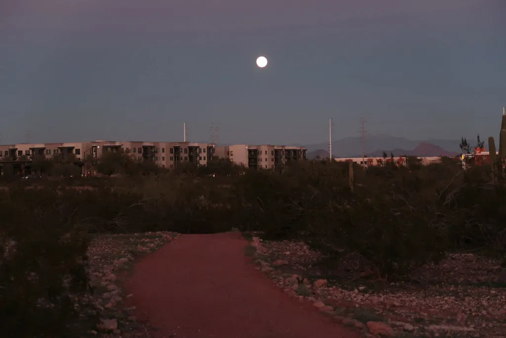 A full moon rising over a desert path and low buildings in Scottsdale