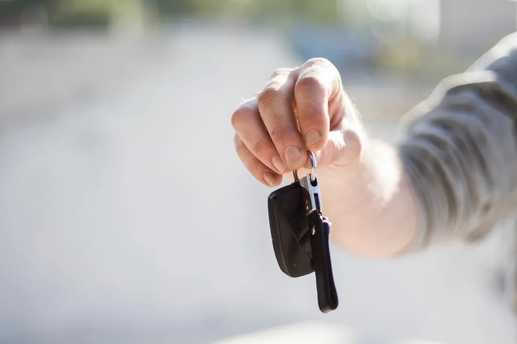 A hand holding a car key with a black remote fob against a pale background