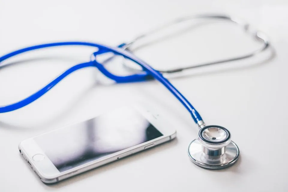 A blue stethoscope lying next to a smartphone on a white surface