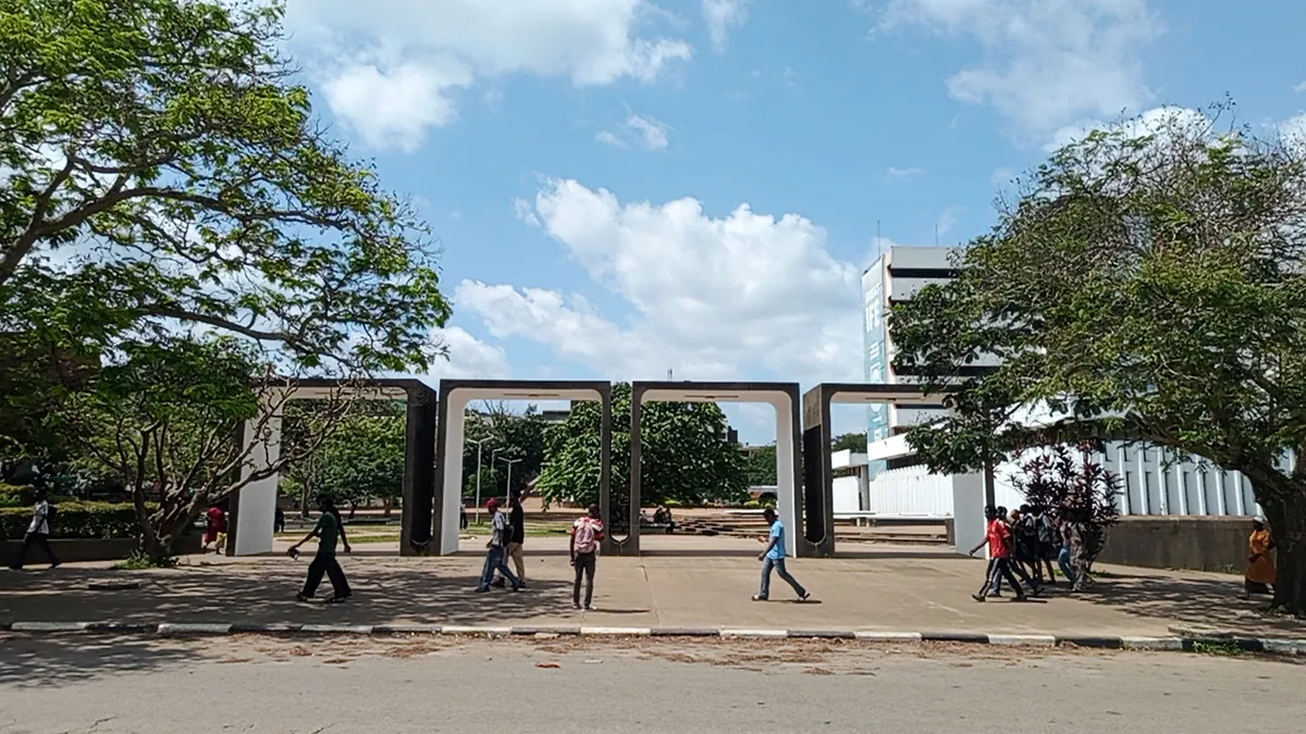 Students walking through a wide concrete gateway on a leafy university campus
