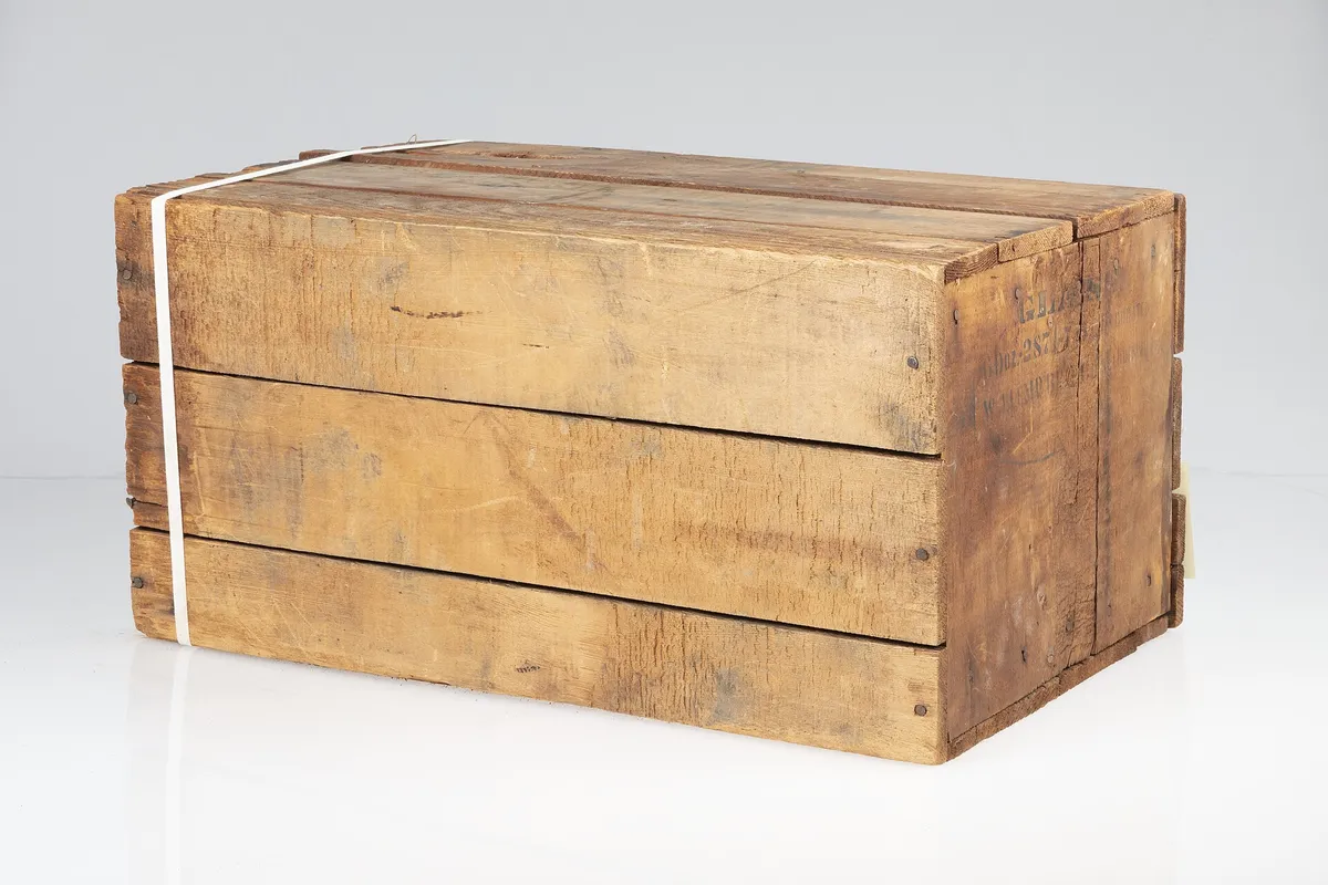 A plain wooden shipping crate held closed with a single white strap
