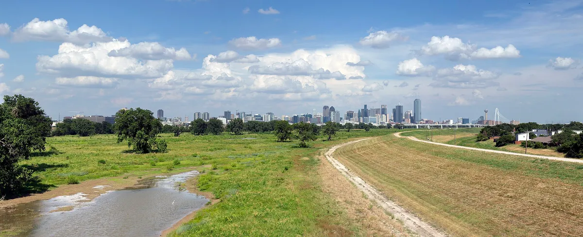 The Dallas skyline on the horizon beyond a grassy Trinity River levee and floodplain