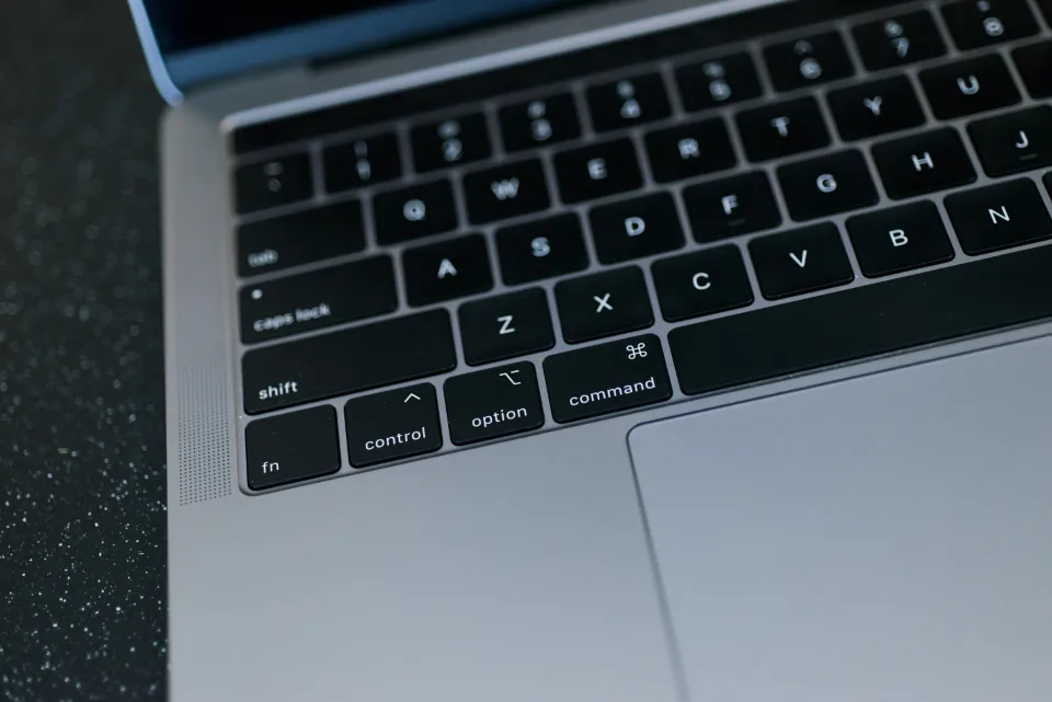 Close-up of a silver laptop keyboard and trackpad on a dark speckled desk