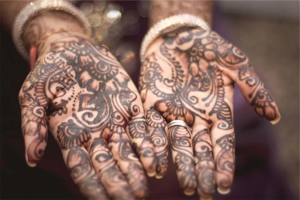 Two open palms decorated with intricate dark henna patterns and a ring