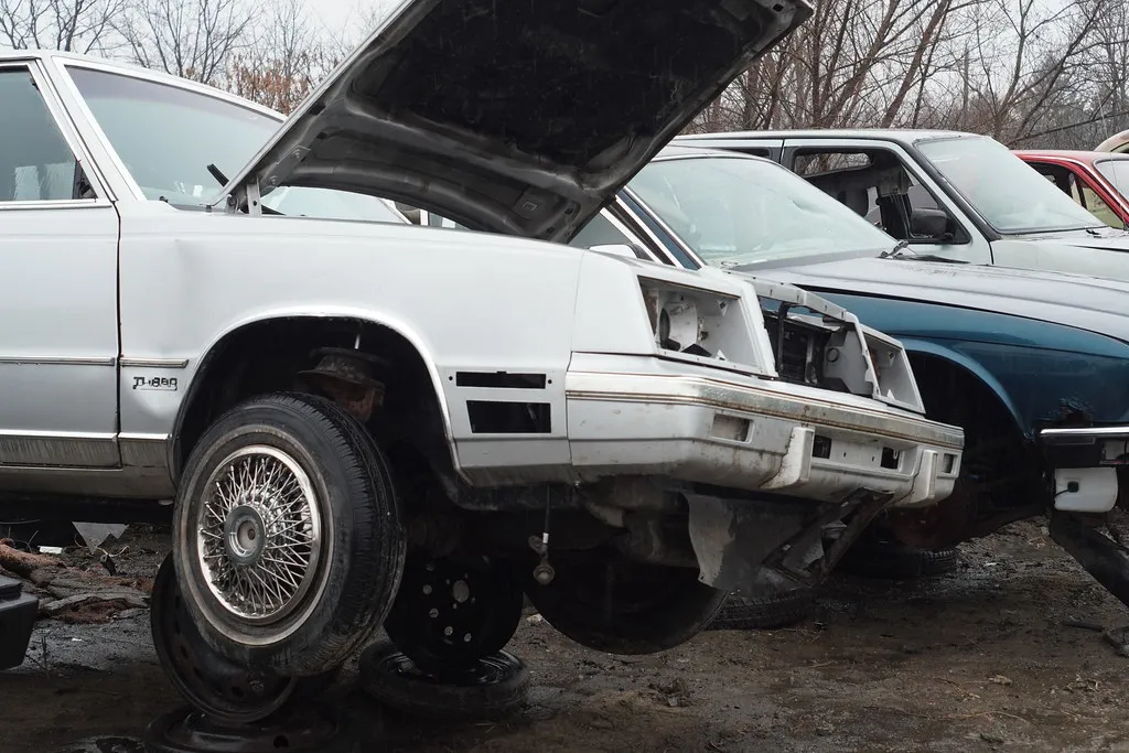 Damaged sedans with crumpled fronts and raised hoods parked in a salvage yard